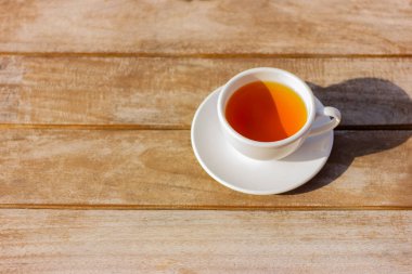 white cup with tea on a saucer on a wooden table in the garden on a sunny day with copy space