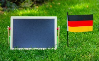 close up black blank chalk board and flag of Germany on green lawn. place for text, copy space.