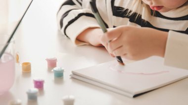 Küçük kız ressam boya ve fırçalarla resim çiziyor. Evde çocuk hobisi yaratıcı sanat aktivitesi yalnız oyna, seçici odaklan, bulanık.