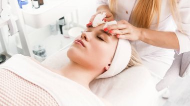 Beautician cosmetologist cleanses the skin of face before professional  cosmetic procedure in a beauty clinic salon for client. Skincare and cosmetology spa concept.