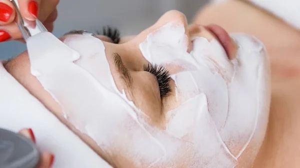 Beautician cosmetologist applying face peeling beauty mask. professional  cosmetic procedure in a beauty clinic salon for client. Skincare and cosmetology spa concept.