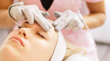 Güzellik uzmanı kozmetik uzmanı, mikroakım terapi eldivenleriyle yüzünden bir prosedür uyguluyor. Klinikte müşteri için donanım kozmetolojisi. 
