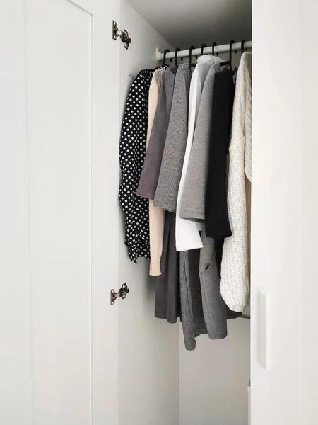 Wardrobe with basic clothes in room scandi interior. Neutral colors: white, black, beige.