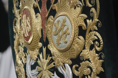 Embroidery thread of gold on green velvet with the acronym for Christ and Mary clipart