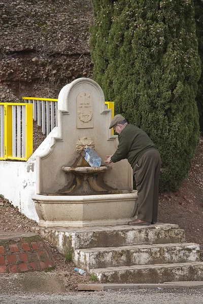 Alter Mann füllt eine Flasche Trinkwasser in einen Brunnen — Stockfoto