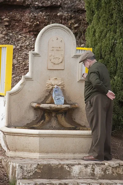 Old man filling a bottle of drinking water in a fountain