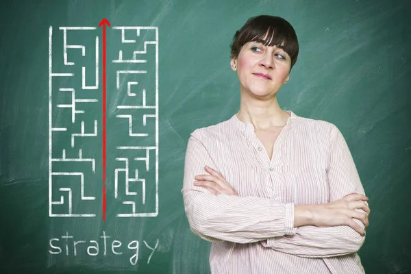 Woman smiles writes on a blackboard the concept of strategy — Stock Photo, Image