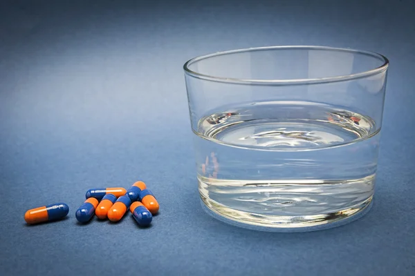 Vaso de agua y pastillas aisladas en azul — Foto de Stock