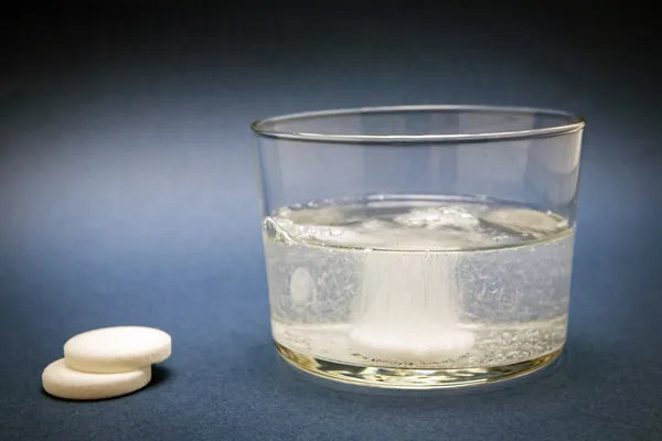 Musujące tabletki do szklanki wody na niebieskim tle — Zdjęcie stockowe