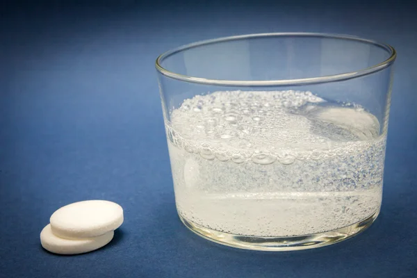 Comprimido efervescente em vidro de água isolado em azul — Fotografia de Stock