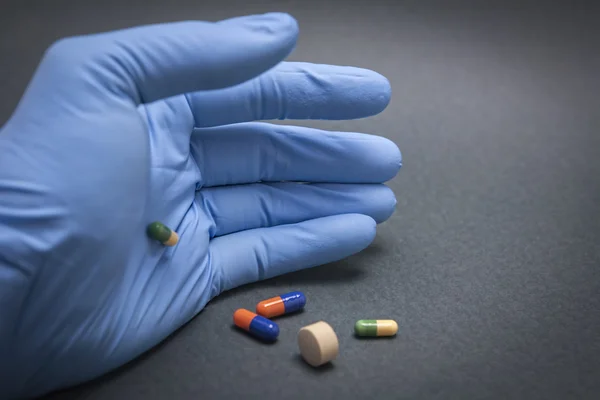 Hand with blue latex glove turning various pills — Stock Photo, Image