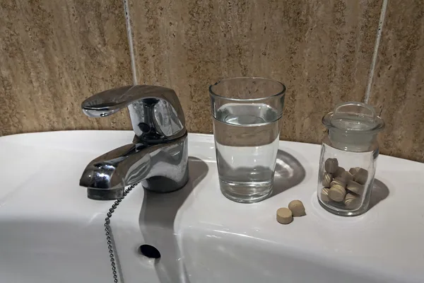 Verre d'eau et pile de plaquettes thermoformées dans l'étagère de la salle de bain — Photo