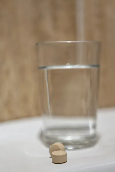Стакан воды и таблетки на полке в ванной комнате — стоковое фото