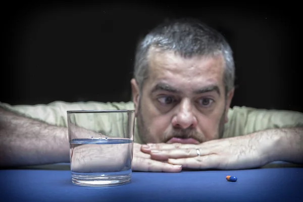 Frustrierter junger Mann sitzt am Tisch und schaut auf die Pille — Stockfoto