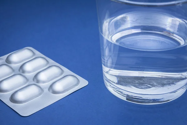 Glass of water and pills isolated on blue — Stock Photo, Image