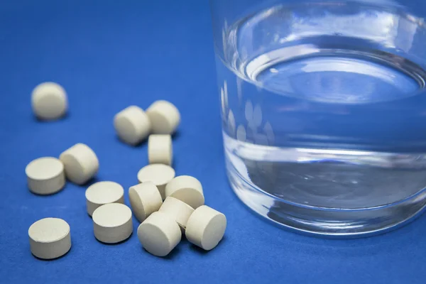 Bicchiere d'acqua e pillole isolate su blu — Foto Stock