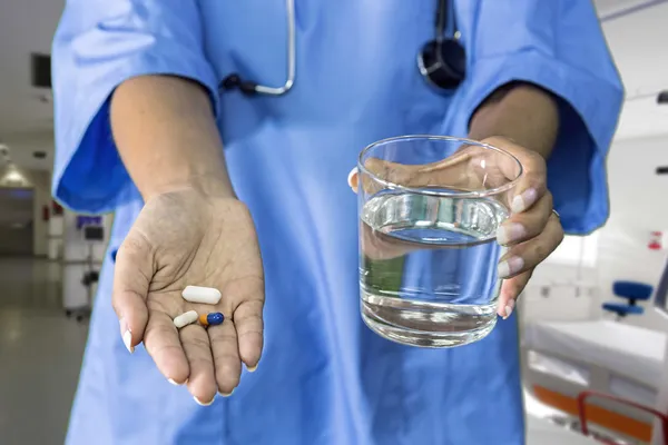 Imagem de mãos de médico dando pílulas brancas e vidro de água — Fotografia de Stock