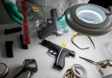 Polis bilimadamı, suç laboratuarı araştırması için çantadan ateşli silah kanıtı çıkardı.