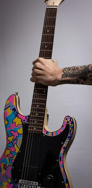 Tatuerade arm och håll en färgad gitarr Stockfoto