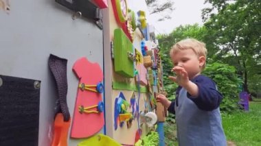 A happy child plays with educational toys in the playground in summer. Wooden game board. Copy space - entertainment concept, bright board for children, kindergarten, fine motor skills of fingers