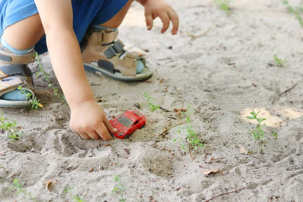 The hand of a little boy and a car model in the sand on the playground. The development of fine motor skills in a small child. Copy space - entertainment concept, role play, leisure, walk.