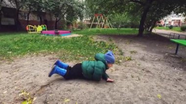 Küçük bir çocuk bir sonbahar günü oyun alanında yürür. Çocuk düşer ve tekrar ayağa kalkar. Boşluğu kopyala - yürümeyi öğrenme kavramı, engeller, bağımsızlık, ilk adımlar, yağmurlu hava, kayma