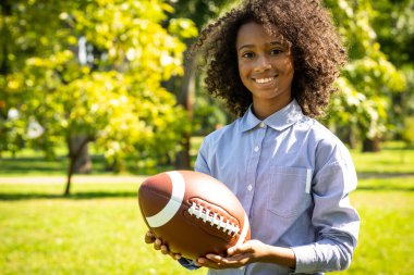 Emirliklerden bir ailenin parkta vakit geçirmesinin sinematik görüntüsü. Erkek ve kız kardeş çimenlerde futbol oynuyorlar.