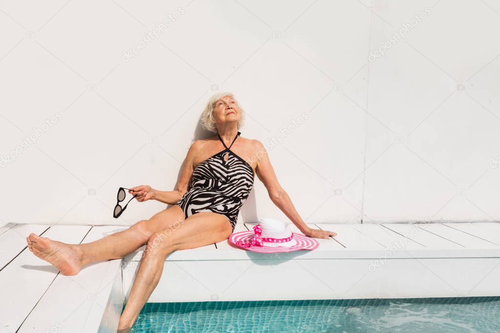 Happy senior woman having party in the swimming pool - Beautiful senior lady sunbathing and relaxing in a private pool during summertime