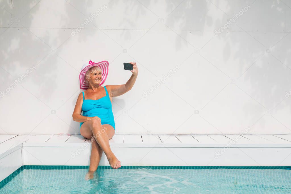 Happy senior woman having party in the swimming pool - Beautiful senior lady sunbathing and relaxing in a private pool during summertime