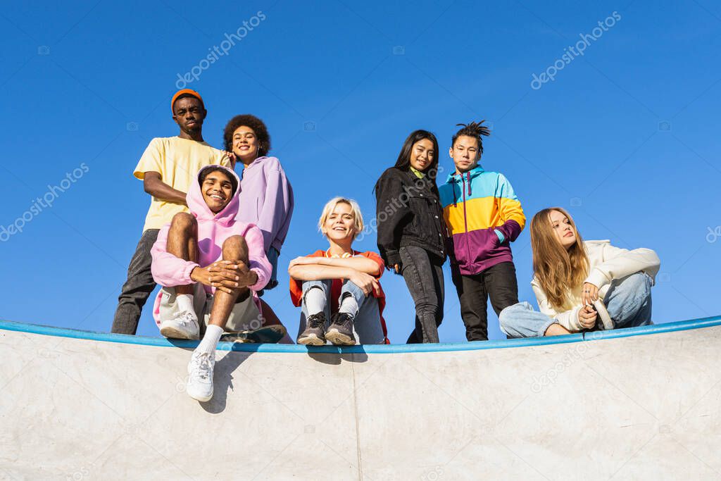 Multicultural group of young friends bonding outdoors and having fun - Stylish cool teens gathering at urban skate park