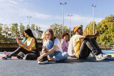 Multicultural group of young friends bonding outdoors and having fun - Stylish cool teens gathering at urban skate park clipart