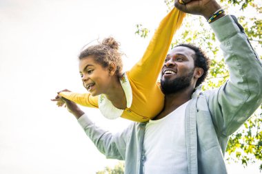 Güzel, mutlu, Afro-Amerikan aile parkta kaynaşıyor, siyahi aile dışarıda eğleniyor, babası tatlı kızıyla oynuyor.