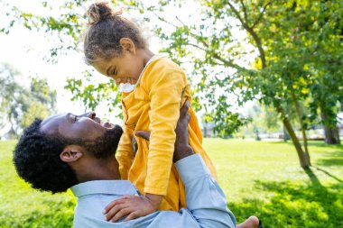 Güzel, mutlu, Afro-Amerikan aile parkta kaynaşıyor, siyahi aile dışarıda eğleniyor, babası tatlı kızıyla oynuyor.