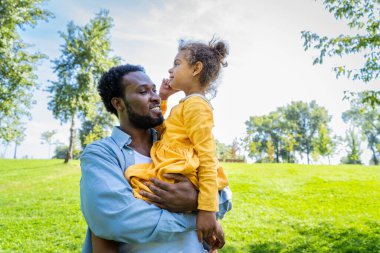 Güzel, mutlu, Afro-Amerikan aile parkta kaynaşıyor, siyahi aile dışarıda eğleniyor, babası tatlı kızıyla oynuyor.