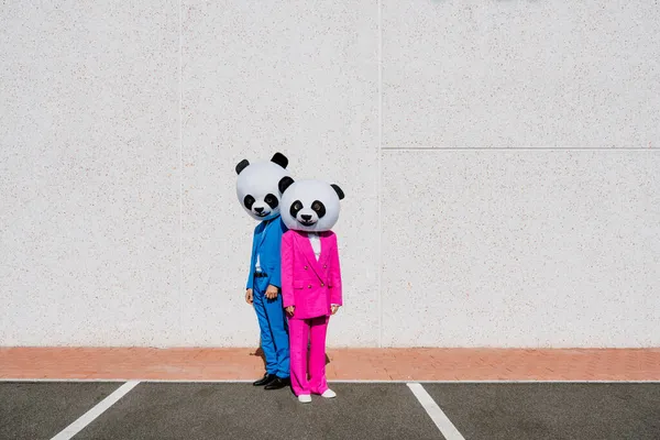 パンダの頭と色付きのスーツを着たカップルの物語のイメージ 駐車場でパーティーをする男と女 — ストック写真