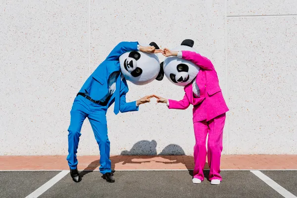 パンダの頭と色付きのスーツを着たカップルの物語のイメージ 駐車場でパーティーをする男と女 — ストック写真