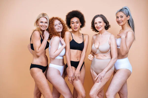 Farklı yaş, ten ve vücutta vücut pozitifliği için poz veren bir grup kadının güzel görüntüsü. Renkli arka planlarda iç çamaşırlı kadın modeller.