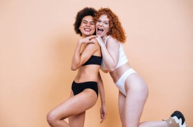 Stüdyoda pozitiflik için poz veren farklı ten ve vücuda sahip iki genç kadının güzel görüntüsü. Renkli arka planlarda iç çamaşırlı kadın modeller.