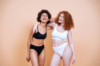 Stüdyoda pozitiflik için poz veren farklı ten ve vücuda sahip iki genç kadının güzel görüntüsü. Renkli arka planlarda iç çamaşırlı kadın modeller.