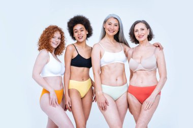 Farklı yaş, ten ve vücutta vücut pozitifliği için poz veren bir grup kadının güzel görüntüsü. Renkli arka planlarda iç çamaşırlı kadın modeller.