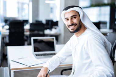 Dubai 'deki ofisinde çalışan yakışıklı bir adam. Geleneksel emirlik beyaz elbiseli başarılı bir iş adamının portreleri. Ortadoğu kültürleri, yaşam tarzı ve meslekleri hakkında kavram