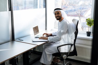 Dubai 'deki ofisinde çalışan yakışıklı bir adam. Geleneksel emirlik beyaz elbiseli başarılı bir iş adamının portreleri. Ortadoğu kültürleri, yaşam tarzı ve meslekleri hakkında kavram