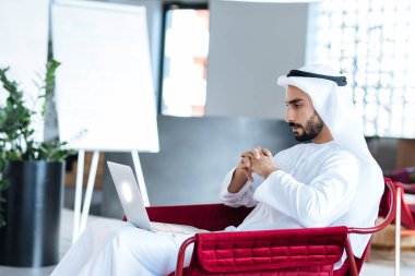 Dubai 'deki ofisinde çalışan yakışıklı bir adam. Geleneksel emirlik beyaz elbiseli başarılı bir iş adamının portreleri. Ortadoğu kültürleri, yaşam tarzı ve meslekleri hakkında kavram
