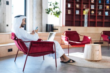 Dubai 'deki ofisinde çalışan yakışıklı bir adam. Geleneksel emirlik beyaz elbiseli başarılı bir iş adamının portreleri. Ortadoğu kültürleri, yaşam tarzı ve meslekleri hakkında kavram