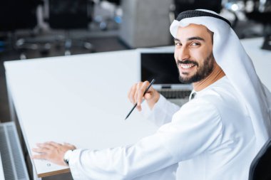 Dubai 'deki ofisinde çalışan yakışıklı bir adam. Geleneksel emirlik beyaz elbiseli başarılı bir iş adamının portreleri. Ortadoğu kültürleri, yaşam tarzı ve meslekleri hakkında kavram
