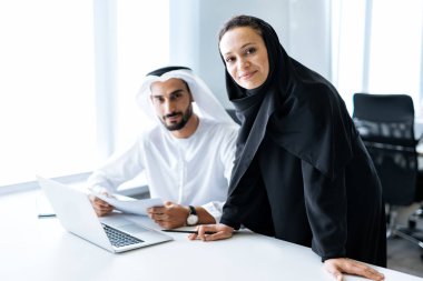Geleneksel kıyafetleri olan bir adam ve kadın Dubai 'de bir iş ofisinde çalışıyor. Başarılı girişimcilerin portreleri iş kadını ve iş kadını resmi emirlik kıyafetleri içinde. Ortadoğu kültürleri, yaşam tarzı ve profesyonel meşguliyeti kavramı