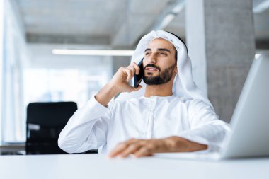 Dubai 'deki ofisinde çalışan yakışıklı bir adam. Geleneksel emirlik beyaz elbiseli başarılı bir iş adamının portreleri. Ortadoğu kültürleri, yaşam tarzı ve meslekleri hakkında kavram