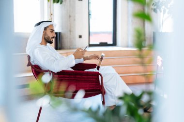 Dubai 'deki ofisinde çalışan yakışıklı bir adam. Geleneksel emirlik beyaz elbiseli başarılı bir iş adamının portreleri. Ortadoğu kültürleri, yaşam tarzı ve meslekleri hakkında kavram