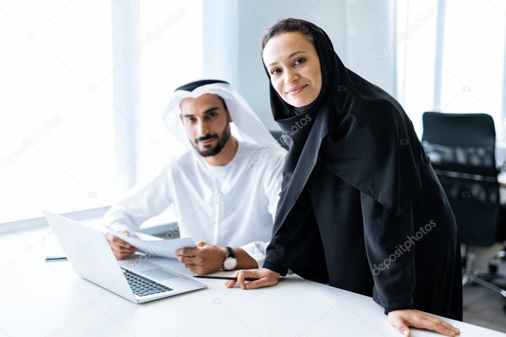 Man and woman with traditional clothes working in a business office of Dubai. Portraits of  successful entrepreneurs businessman and businesswoman in formal emirates outfits. Concept about middle eastern cultures, lifestyle and professional occupatio