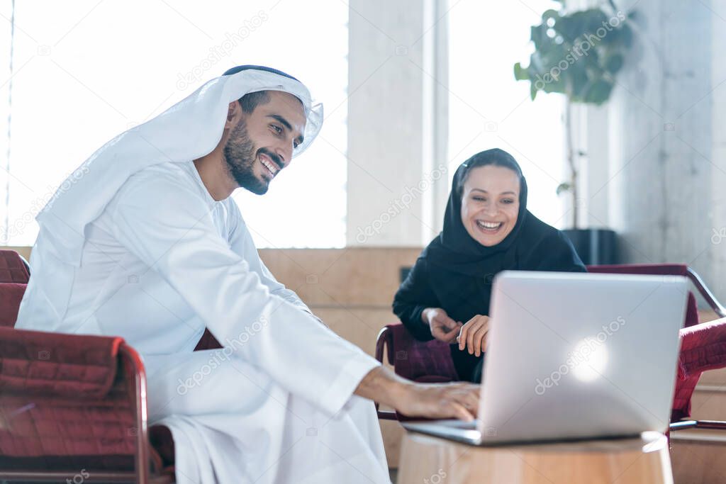 Man and woman with traditional clothes working in a business office of Dubai. Portraits of  successful entrepreneurs businessman and businesswoman in formal emirates outfits. Concept about middle eastern cultures, lifestyle and professional occupatio